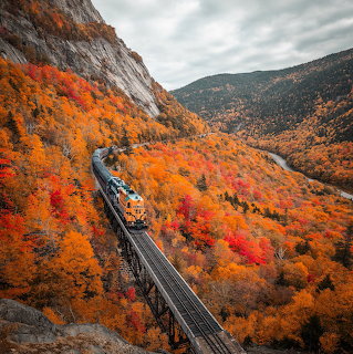 Blue train on a bridge winding through bright autumn forest in a mountain valley