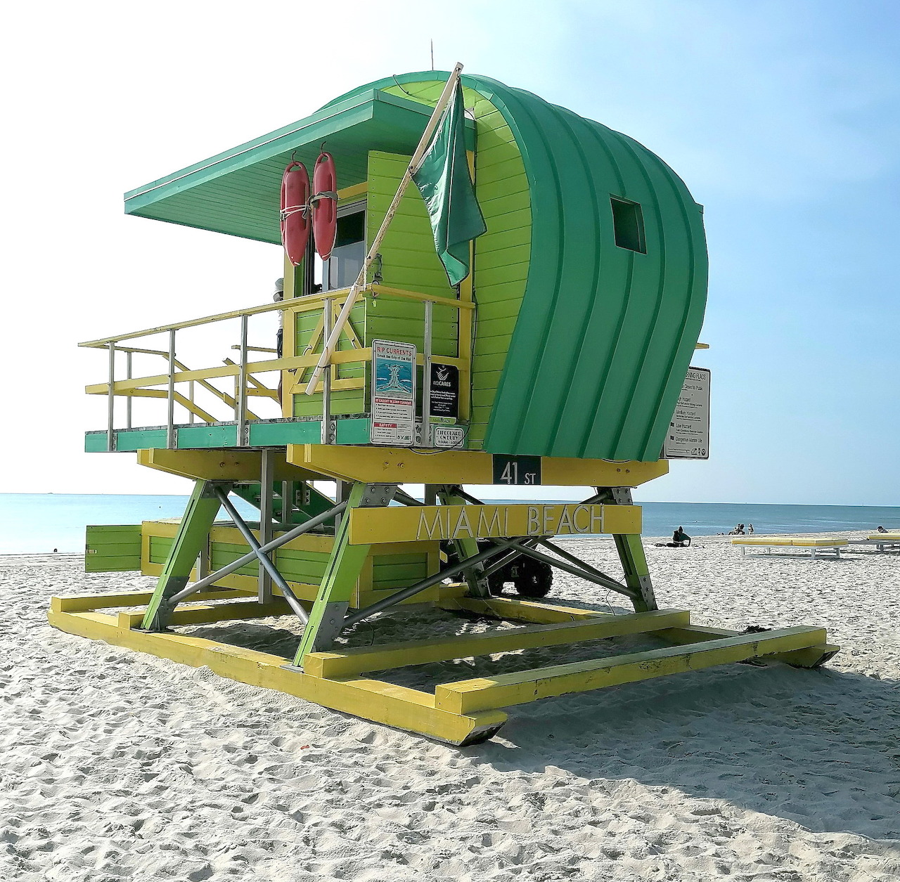 Bright green lifeguard tower on a sandy beach with ocean and blue sky