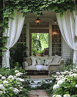 Covered garden porch with white draping curtains, wicker sofa, green vines, and white roses