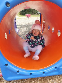 Smiling child in pink hat sitting inside bright orange playground tunnel with blue trim
