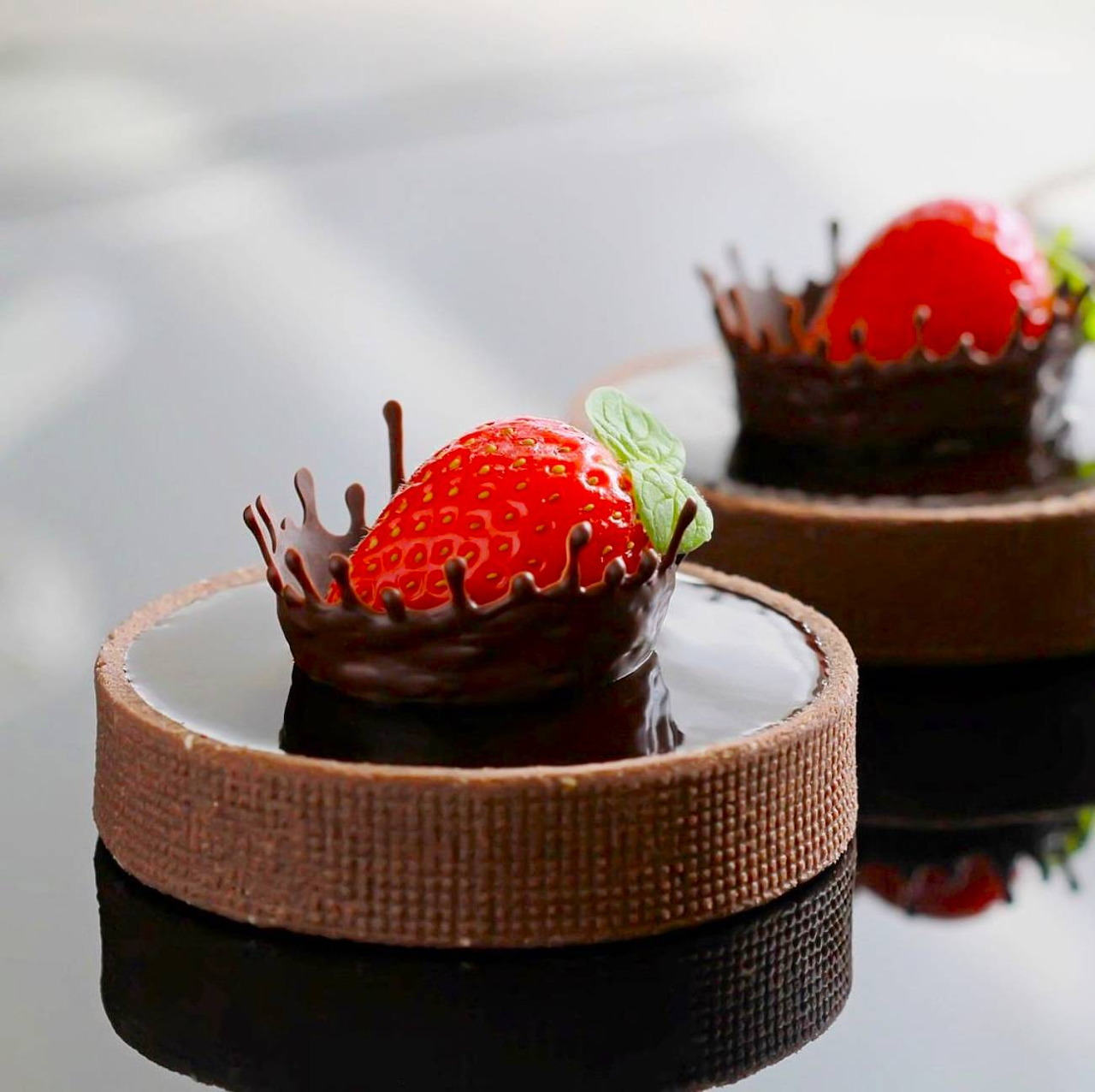 Two chocolate desserts with strawberries and chocolate decorations on white surface