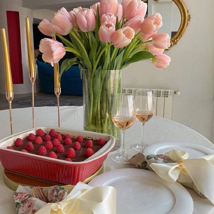 Pink tulips in glass vase with raspberries, wine glasses, and white plates on elegant table