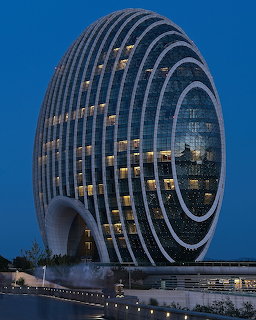 Egg-shaped modern hotel building with curved white ribs illuminated at night against a blue sky
