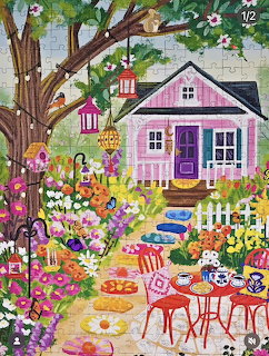 Pink cottage with colorful garden, white fence, tea table, tree with birdhouses, and flowers