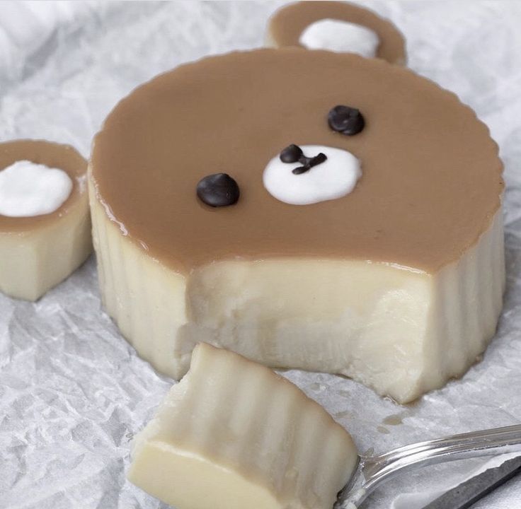 Bear-shaped pudding with caramel face, white cream body, and decorative ears on textured surface