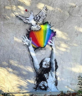 Street art mural showing girl with rainbow heart releasing white dove on gray wall