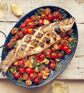 Whole roasted fish on a platter with cherry tomatoes and roasted potatoes