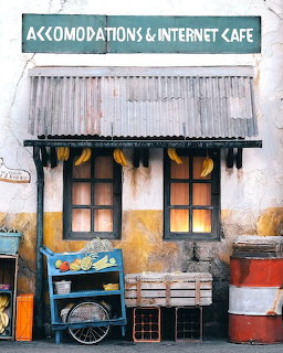 Rustic internet cafe storefront with tin roof, yellow walls, wooden doors, and fruit cart
