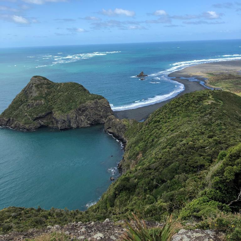 Coastal view of Whatipu Beach with green cliffs, black sand, and blue ocean