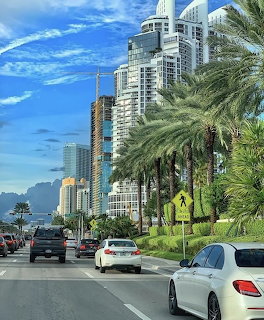 Cars driving on a palm-lined boulevard with high-rise buildings and a construction crane in a tropical city