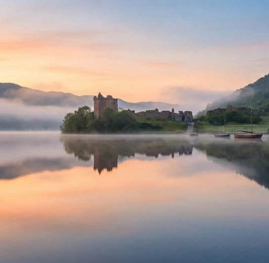 Misty castle by a calm lake at sunrise with soft reflections and a small boat