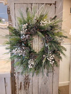 Winter wreath with pinecones, evergreen branches, and white berries on a rustic white wooden door