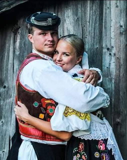 Young couple in traditional folk costumes embracing in front of a wooden wall