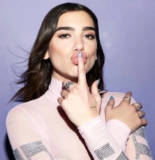 Studio portrait of Dua Lipa posing with finger to lips against a purple background