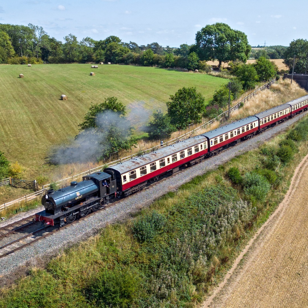 Vintage steam train with red carriages traveling through rural countryside landscape