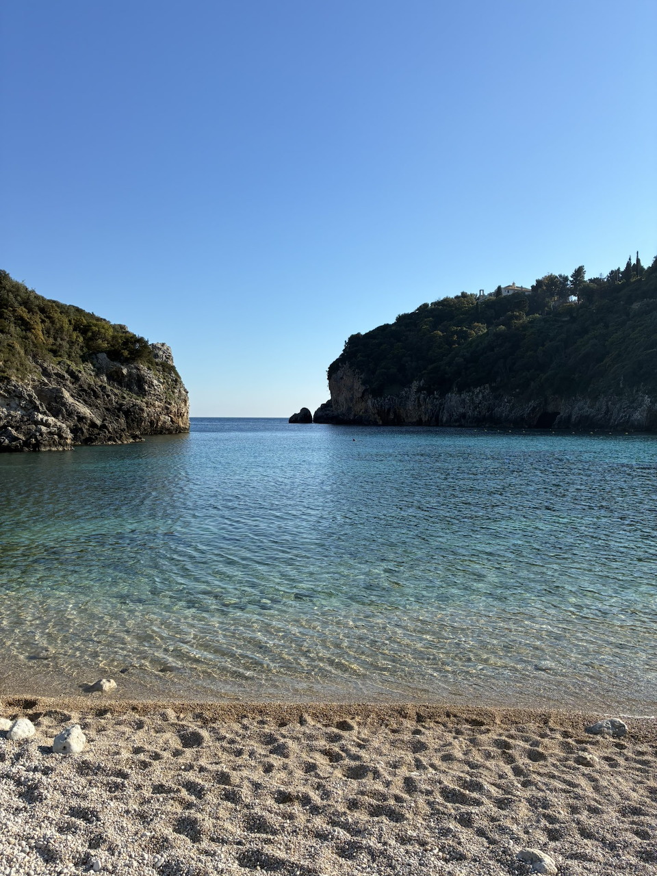 Calm turquoise cove with sandy beach flanked by rocky green headlands under a clear blue sky