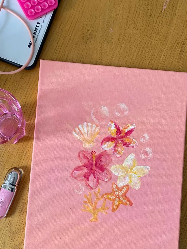 Pink canvas with painted tropical flowers, seashell, starfish, coral, and bubbles on a wooden table