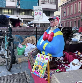 Colorful Donald Duck-style statue at an outdoor street market with bicycles and assorted items