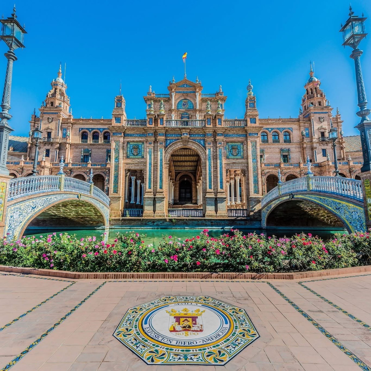 Plaza de España in Seville with ornate facade, twin bridges, flowerbeds, and a tiled emblem