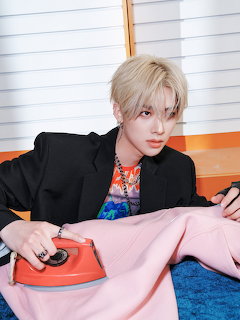 Blond young man using a red iron on a pink garment indoors