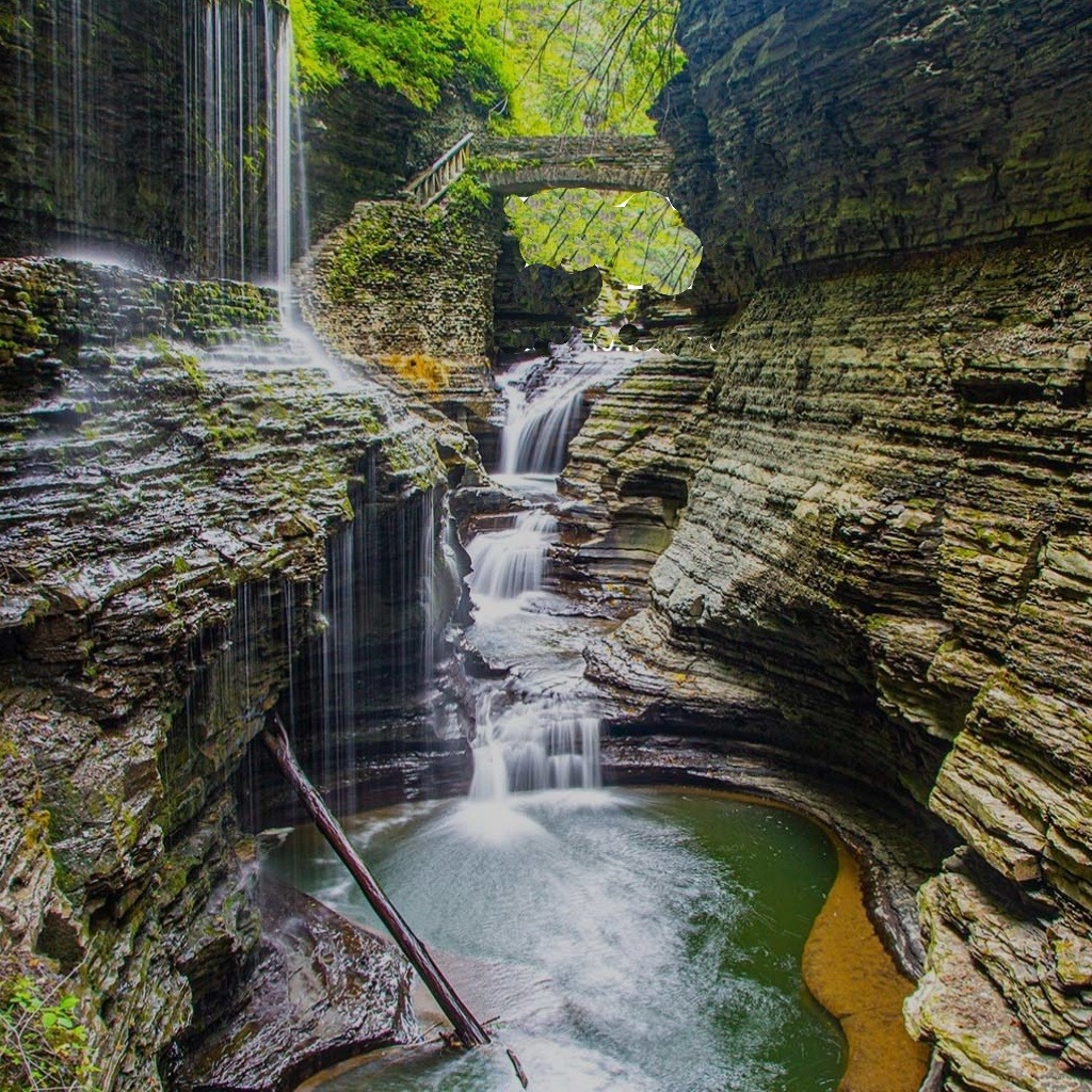 Waterfall flowing through a rocky gorge beneath a small stone bridge