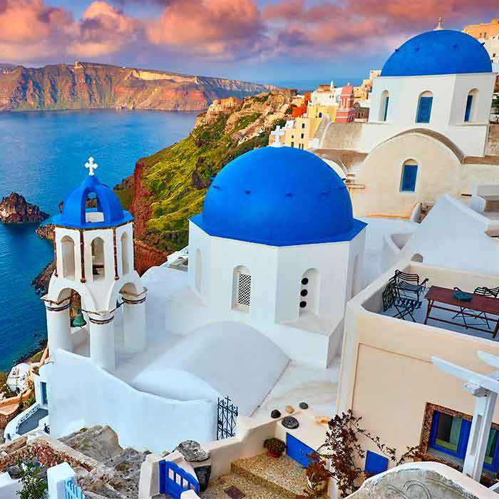 White Greek Orthodox churches with blue domes on cliff overlooking sea at sunset