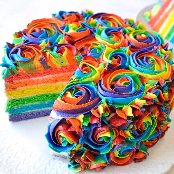 Slice of rainbow layer cake decorated with multicolored frosting swirls and sprinkles