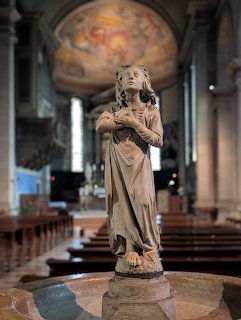 Stone statue inside a church with pews and a frescoed apse behind it