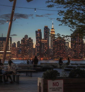 Manhattan skyline at dusk seen from a waterfront deck with people silhouetted against illuminated buildings