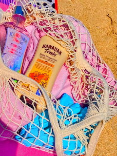 Mesh beach bag on sand with sunscreen bottle, pink towel, and summer accessories