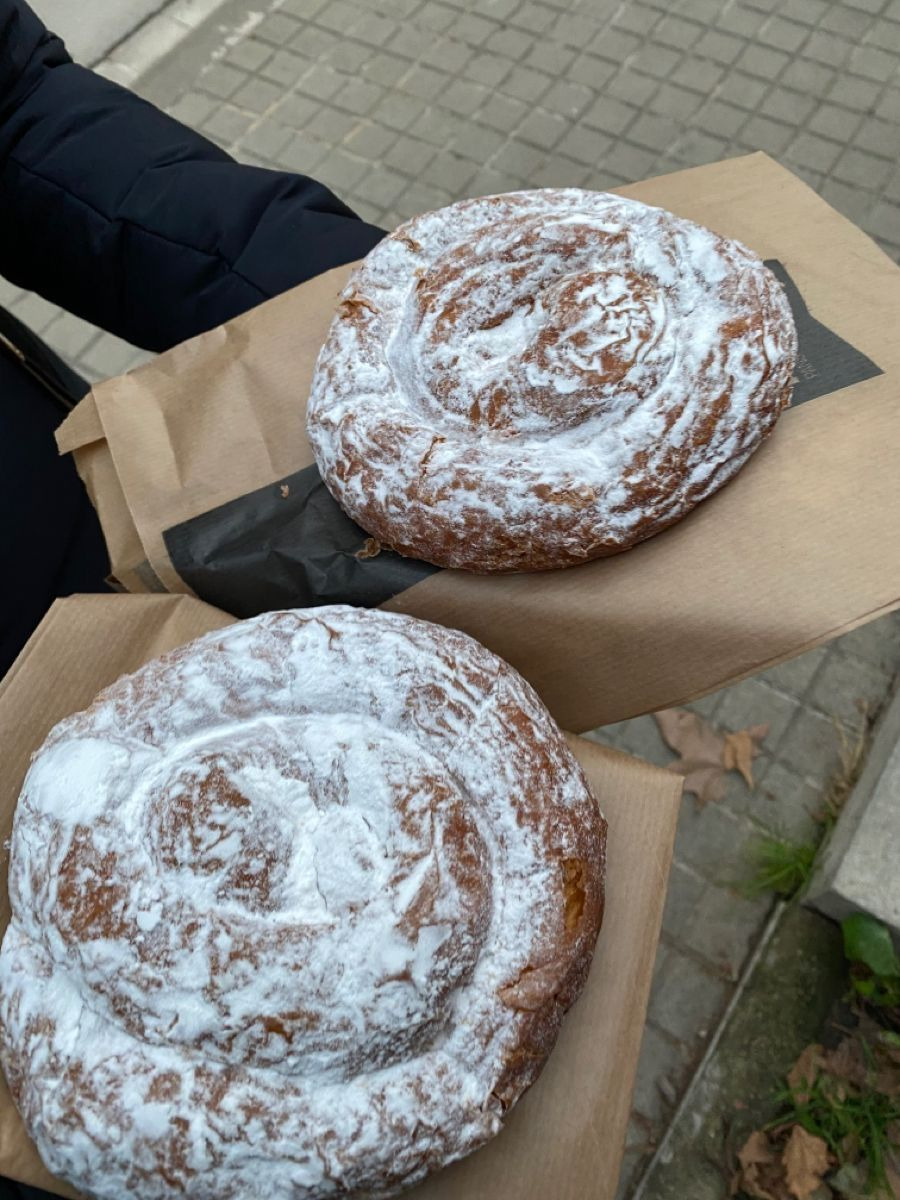 Two ensaimadas dusted with powdered sugar on napkins outdoors