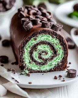Chocolate swiss roll with green mint swirl filling topped with chocolate ganache and chunks on a white plate