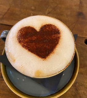 Cappuccino with a heart shape made of cocoa powder on milk foam in a blue cup on a wooden table