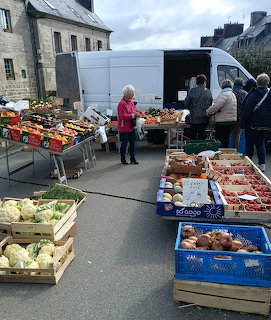 Outdoor French street market with vegetable stalls, wooden crates of produce, and shopers near a white van