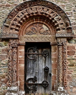 Carved Romanesque church doorway with a weathered wooden door set in a stone wall