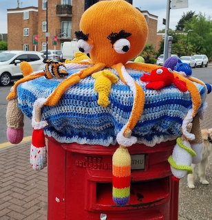 Red post box decorated with a colorful crocheted octopus and knitted sea creatures outdoors