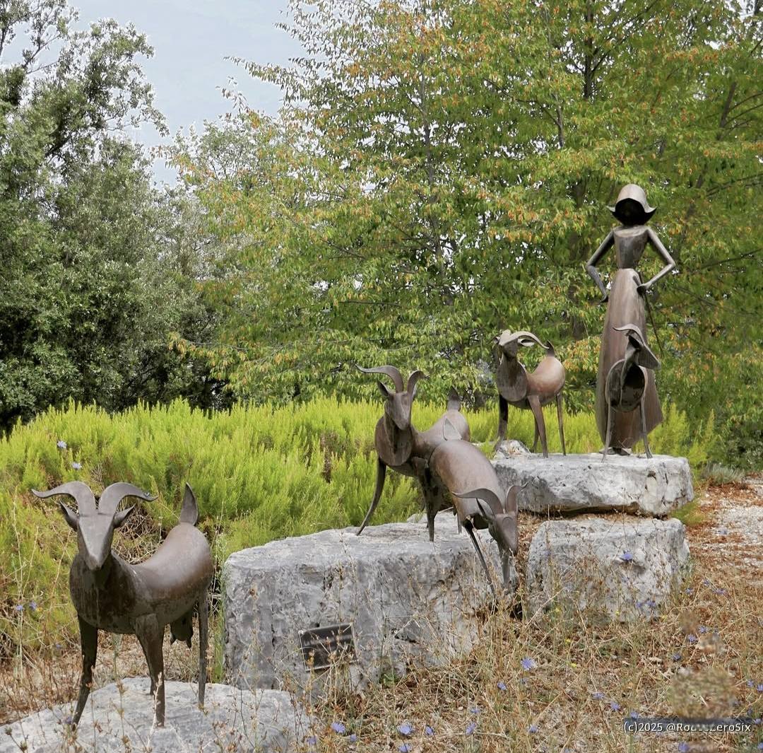 Metal animal and human sculptures displayed on rocks in a green outdoor garden