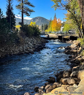 River flowing over rocks through a mountain town with fall foliage and a bridge in the background