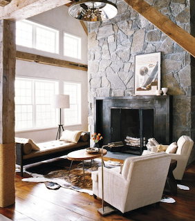 Rustic living room with stone fireplace, wooden beams, cream armchairs, and cowhide rug