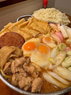 Bowl of miso stewed udon with eggs, noodles, chicken, tofu, fish cake, and scallions