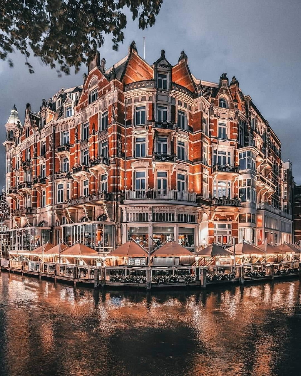 Illuminated Hotel de L'Europe in Amsterdam at dusk with canal reflections