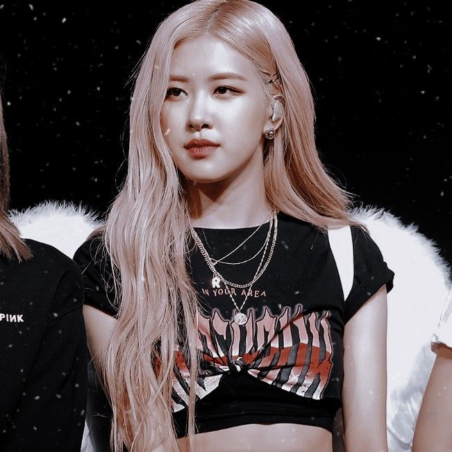 Rosé from Blackpink with long pink hair wearing a black graphic crop top and silver necklaces on stage