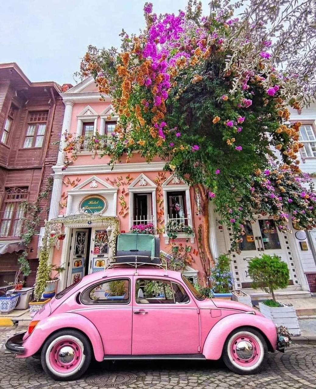 Pink vintage Volkswagen Beetle on cobblestone street in Istanbul with flower-covered buildings