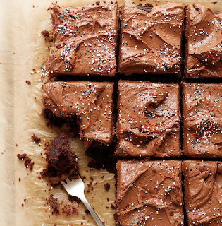 Chocolate brownie squares with frosting and sprinkles on parchment paper next to a fork