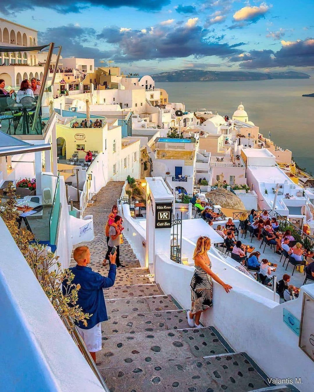 Tourists walking through white buildings on terraced steps in Santorini, Greece at sunset