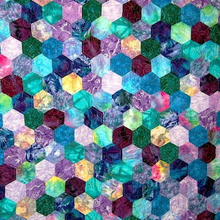 Colorful hexagonal patchwork quilt with teal, purple, pink, and green fabric pieces in repeating geometric pattern