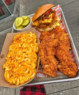 Metal tray with fried chicken, mac and cheese, bacon burger, and pickles on checkered cloth