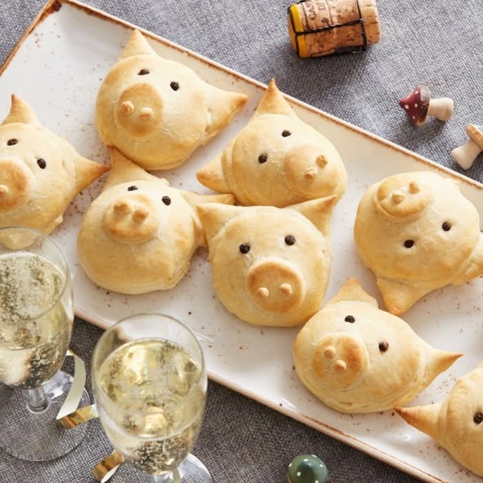 Golden bread rolls shaped like cute piglets on a white serving tray next to a champagne glass