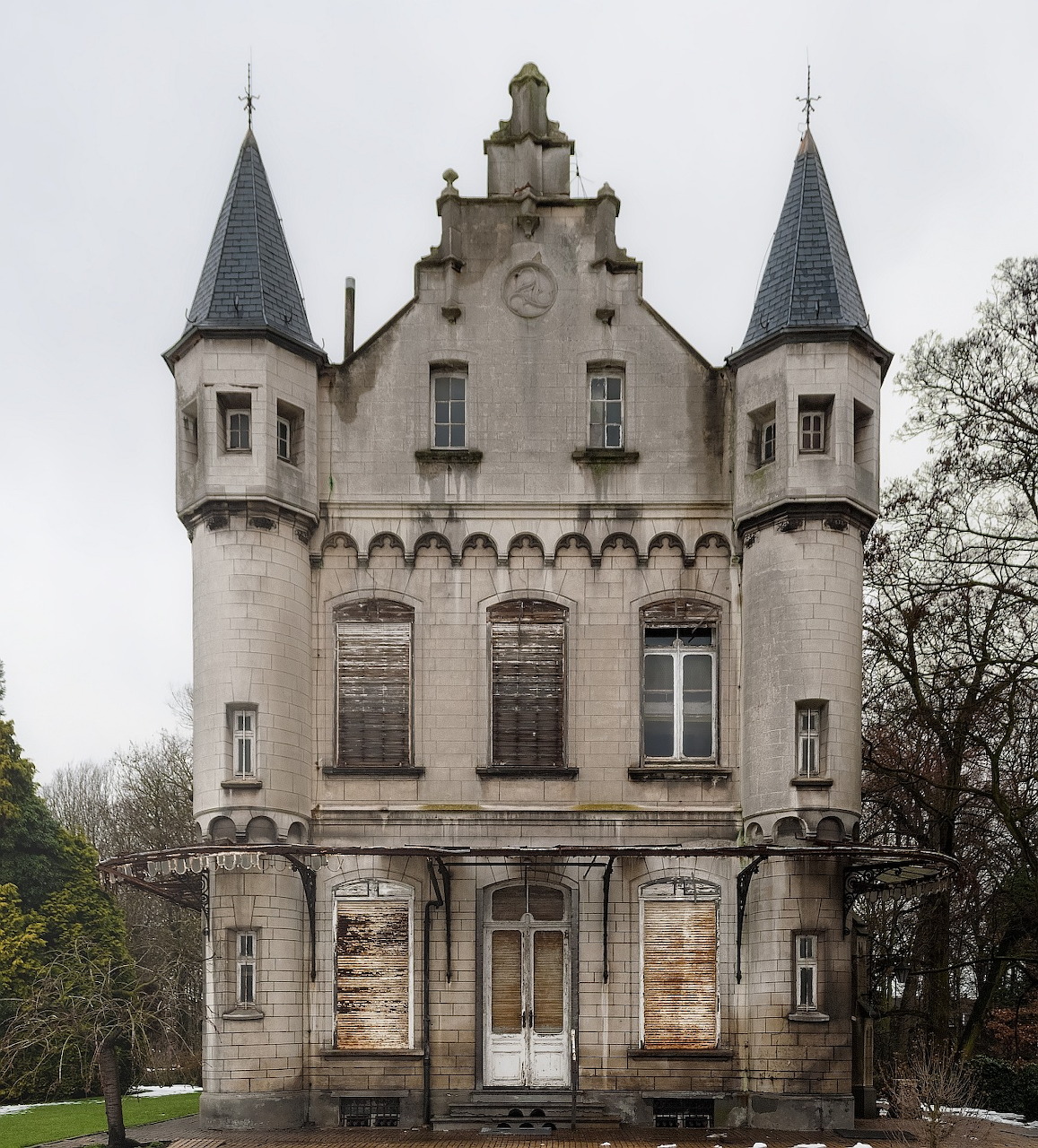 Abandoned Belgian castle with twin conical turrets and ornate stone facade in winter