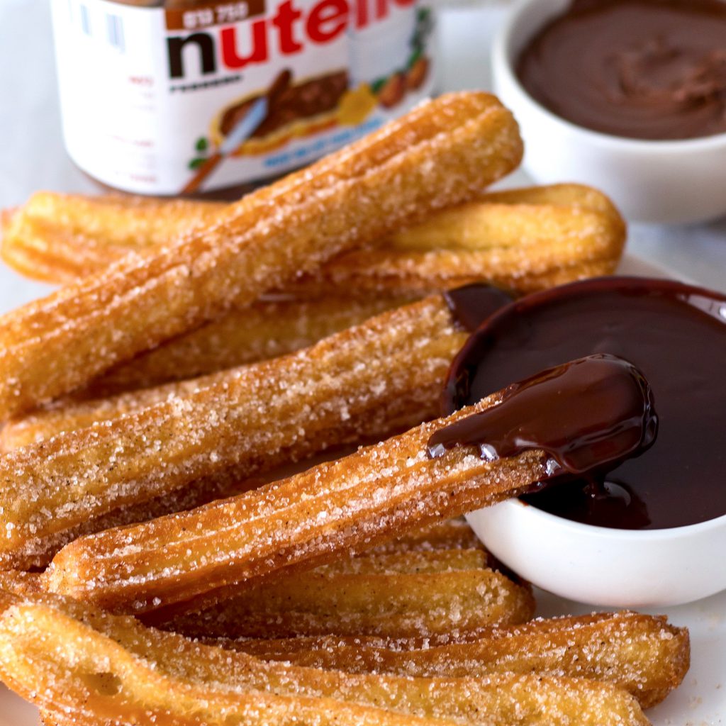 Stack of sugar-coated churros with chocolate dipping sauces in small white bowls
